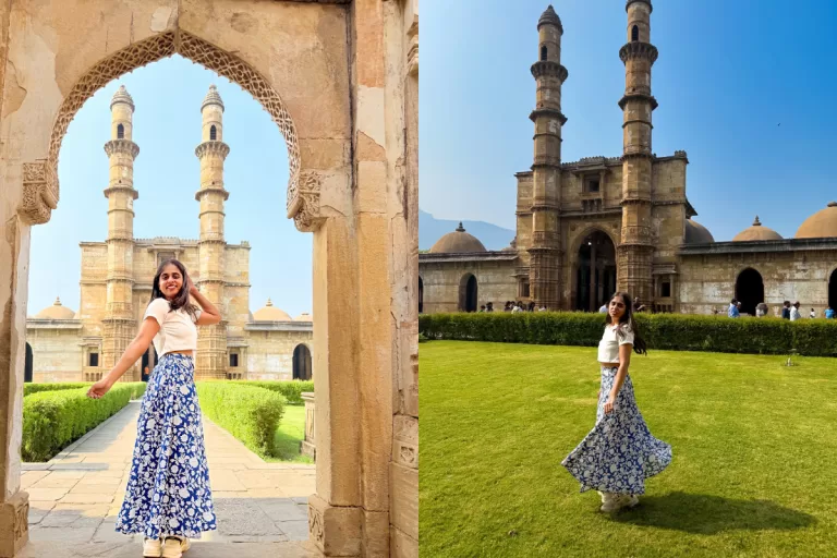A woman posing inside Jama Masjid, Champaner, with ancient stone arches, twin minarets, green lawns, and clear blue sky in the background.