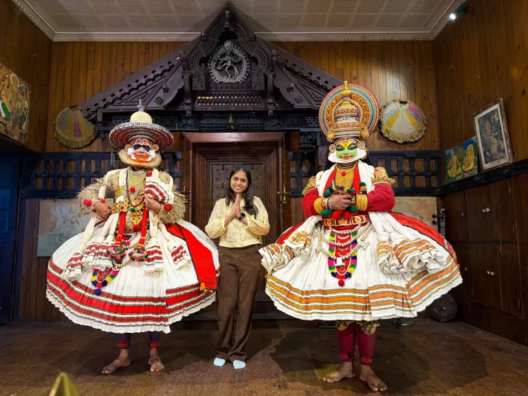 Woman posing with Kathakali artists in traditional costume at Kerala Kathakali Centre in Kochi, showcasing classical dance makeup and attire.