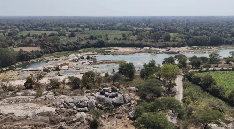 Aerial view of a river flowing through rocky terrain and lush green fields near Gupteshwar Mahadev Temple in Ghusar, Gujarat.