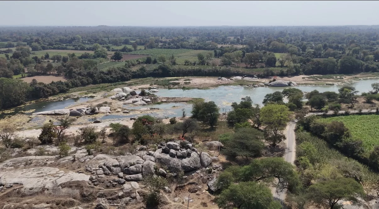 Aerial view of a river flowing through rocky terrain and lush green fields near Gupteshwar Mahadev Temple in Ghusar, Gujarat.