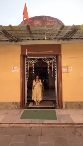 Devotee standing at the entrance of Angareshwar Mahadev Temple with folded hands, decorated temple doorway and saffron flag visible above the dome