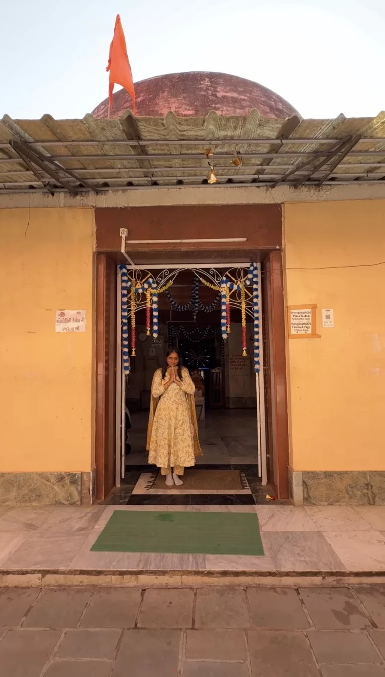 Devotee standing at the entrance of Angareshwar Mahadev Temple with folded hands, decorated temple doorway and saffron flag visible above the dome